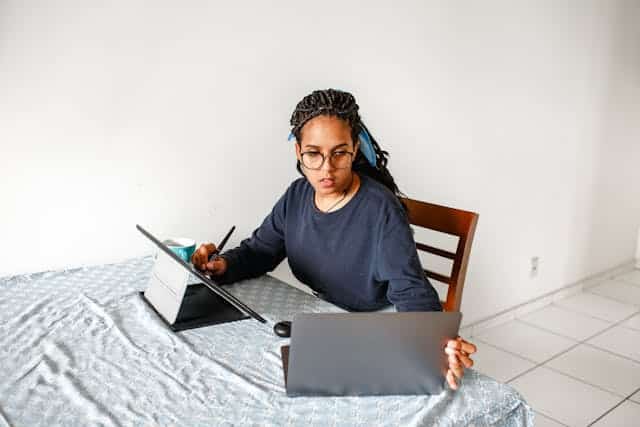 A Women Multitasking Sitting On A Chair With A Laptop And A Tablet