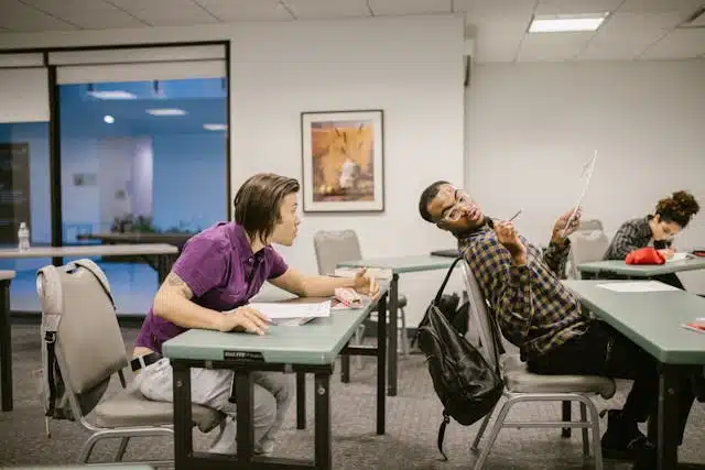 Two students at a desk, one copying code from another student's laptop screen during an assignment