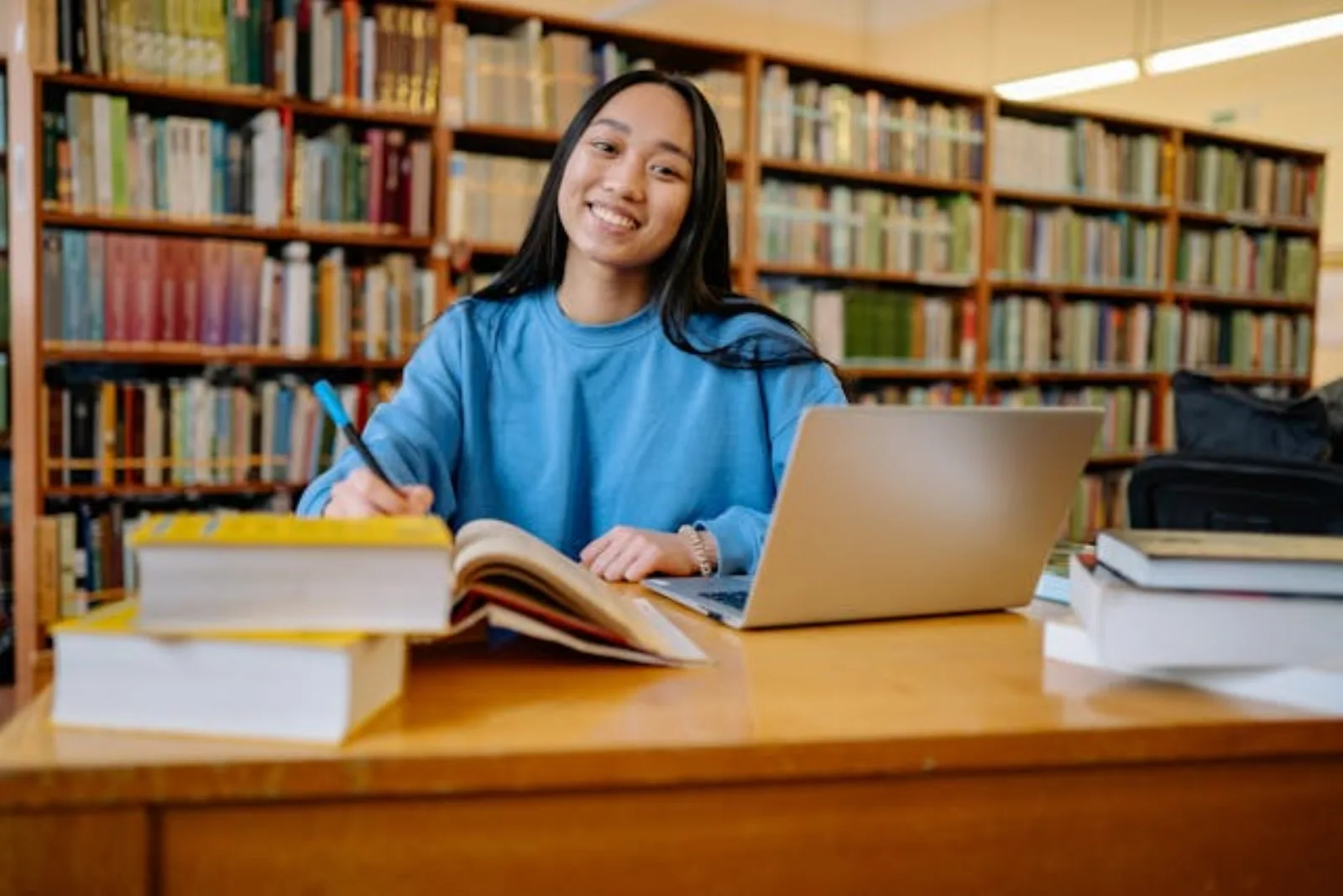 A first-year college student sitting at a desk with a laptop open to a code editor, textbooks stacked beside them, and a phone showing a calendar app